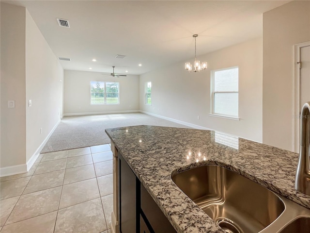 kitchen featuring ceiling fan with notable chandelier, light tile patterned flooring, hanging light fixtures, and stone counters