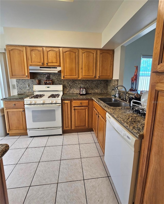 kitchen featuring light tile patterned floors, white appliances, dark stone countertops, and sink