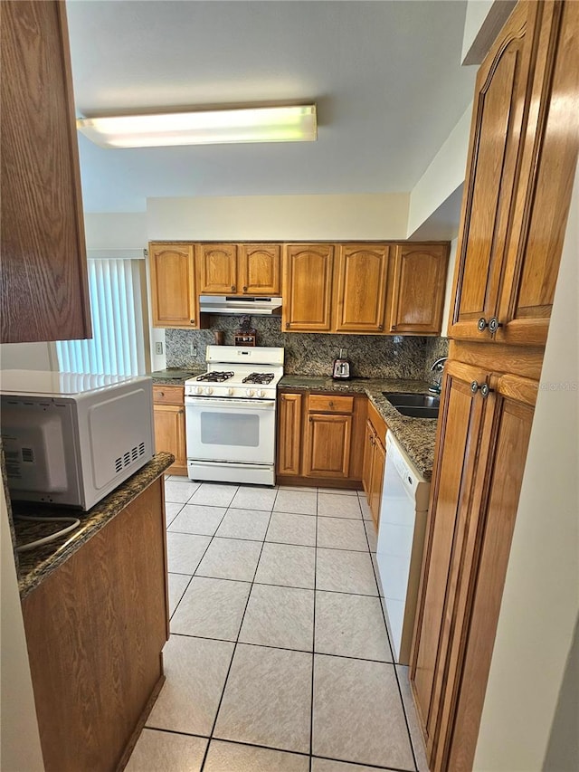 kitchen with white appliances, backsplash, sink, dark stone countertops, and light tile patterned floors