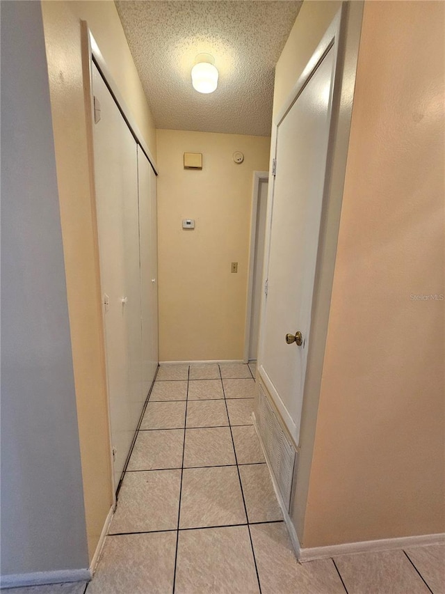 hallway with a textured ceiling and light tile patterned flooring