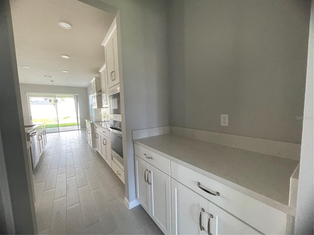 kitchen featuring white cabinetry, hanging light fixtures, built in microwave, and stainless steel oven