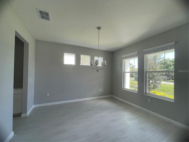 spare room with a notable chandelier, a textured ceiling, and light hardwood / wood-style flooring