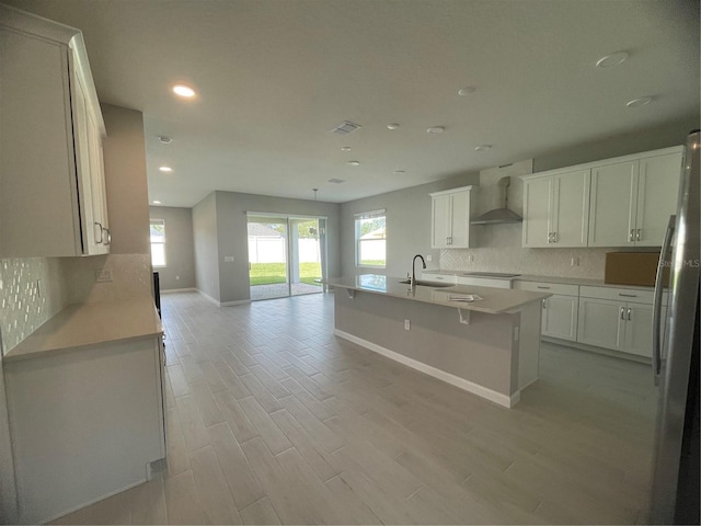 kitchen with tasteful backsplash, white cabinetry, sink, stainless steel fridge, and wall chimney range hood