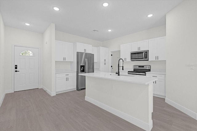 kitchen with appliances with stainless steel finishes, white cabinetry, sink, and a center island with sink