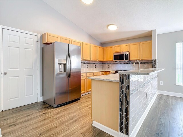 kitchen featuring lofted ceiling, tasteful backsplash, stainless steel appliances, and light hardwood / wood-style floors