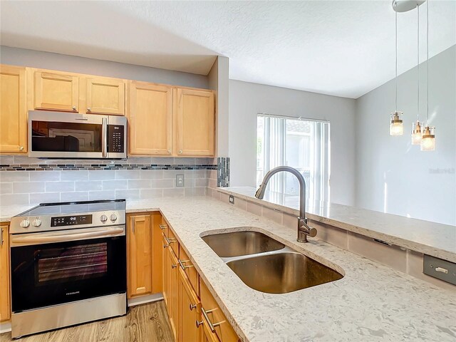 kitchen with light wood-type flooring, hanging light fixtures, appliances with stainless steel finishes, decorative backsplash, and sink