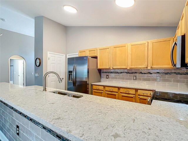 kitchen with stainless steel appliances, sink, light stone counters, backsplash, and high vaulted ceiling