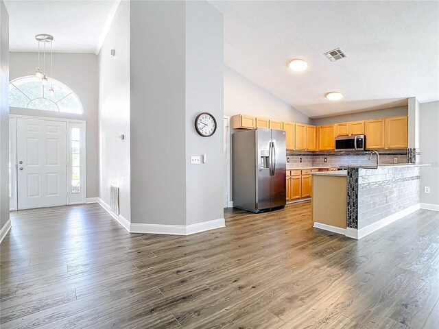 kitchen featuring backsplash, stainless steel appliances, light brown cabinetry, wood-type flooring, and high vaulted ceiling