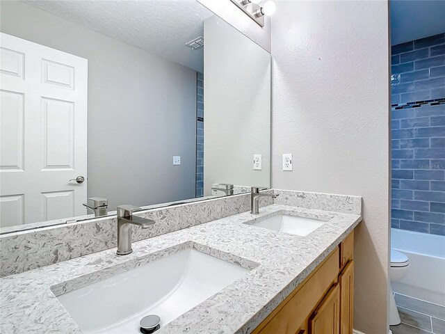 full bathroom featuring double vanity, a textured ceiling, tiled shower / bath, and toilet