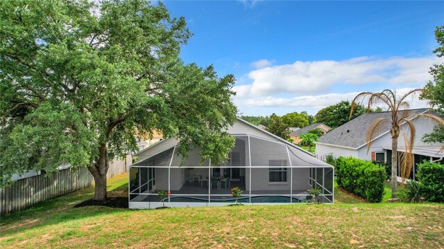 rear view of house featuring glass enclosure, a lawn, and a pool