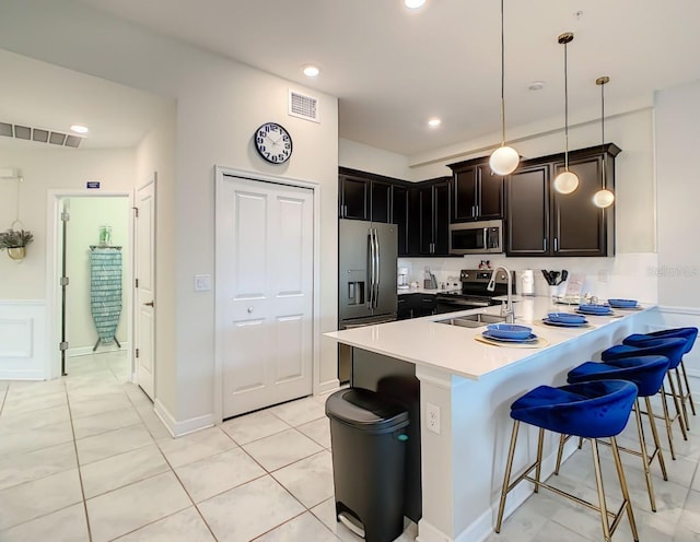 kitchen with stainless steel appliances, a kitchen breakfast bar, kitchen peninsula, pendant lighting, and light tile patterned flooring