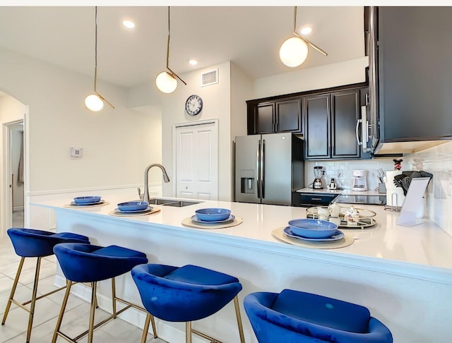 kitchen featuring decorative backsplash, stainless steel fridge, a breakfast bar, sink, and hanging light fixtures