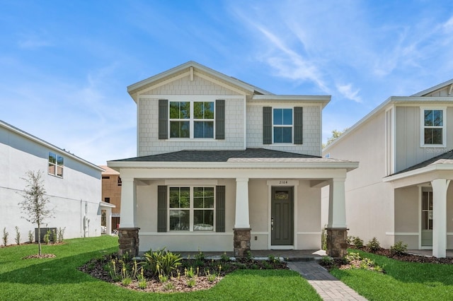 craftsman inspired home with stucco siding, a porch, central AC, a front yard, and a shingled roof