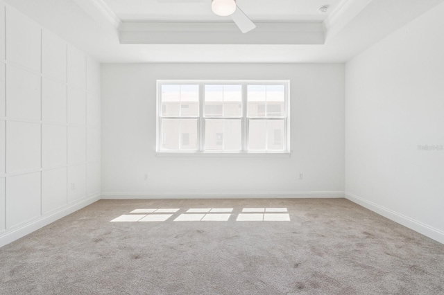 empty room with a raised ceiling, a ceiling fan, light carpet, and crown molding