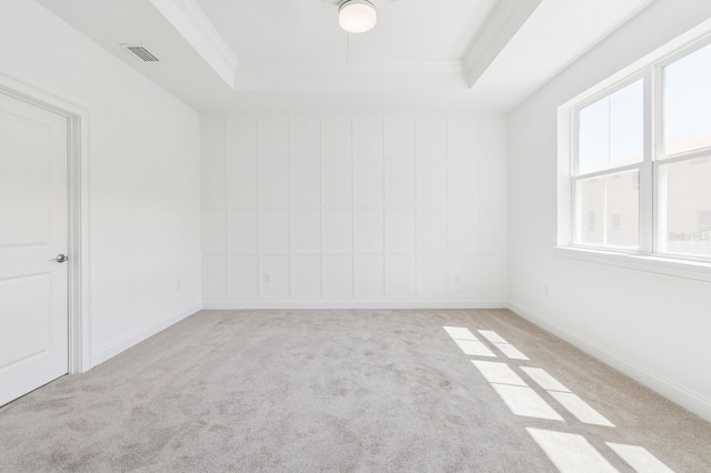 carpeted empty room with a tray ceiling, baseboards, visible vents, and ornamental molding