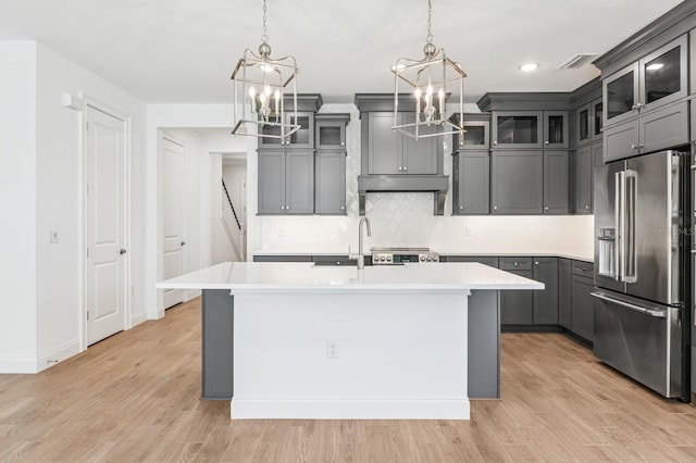 kitchen with gray cabinetry, light countertops, light wood-style floors, stainless steel appliances, and a kitchen island with sink