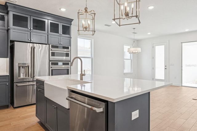 kitchen with wood finish floors, visible vents, a kitchen island with sink, a sink, and appliances with stainless steel finishes