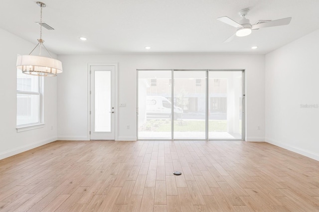 unfurnished living room with visible vents, baseboards, light wood-style floors, and ceiling fan with notable chandelier