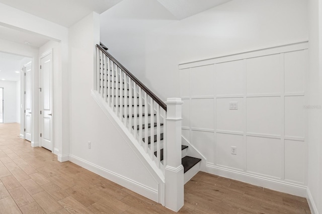 staircase featuring a decorative wall, wood finished floors, and baseboards