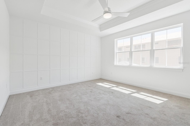 empty room featuring carpet flooring, baseboards, a raised ceiling, and ceiling fan