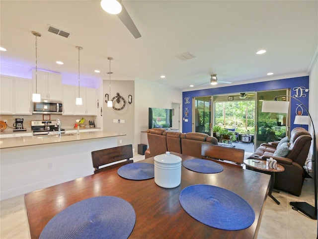 tiled dining area with crown molding, sink, and ceiling fan