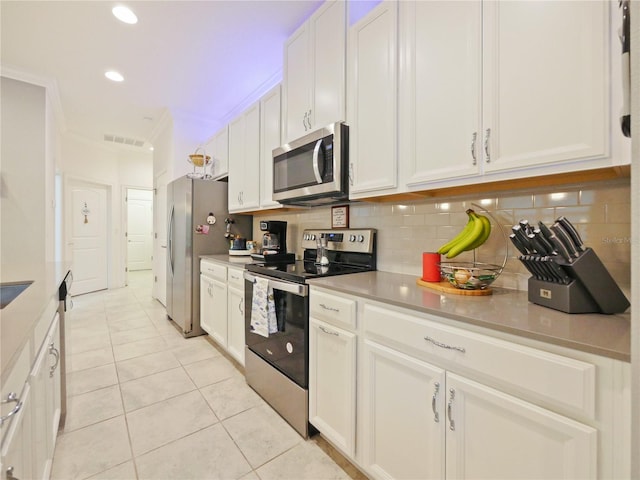 kitchen with tasteful backsplash, light tile floors, ornamental molding, white cabinets, and appliances with stainless steel finishes