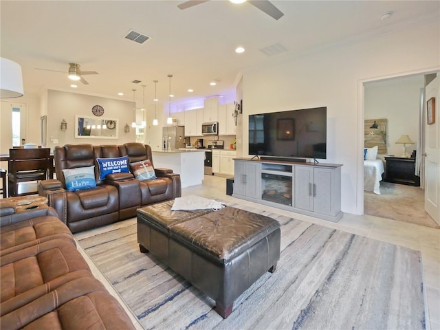 living room featuring crown molding, ceiling fan, a fireplace, and light tile flooring