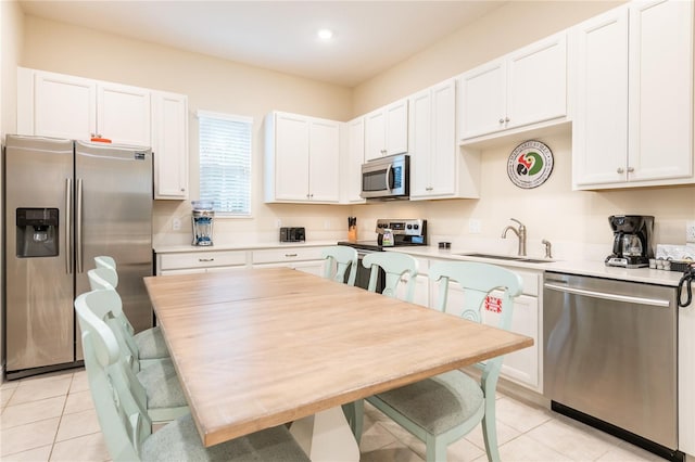 kitchen with white cabinetry, sink, stainless steel appliances, a kitchen breakfast bar, and light tile patterned flooring