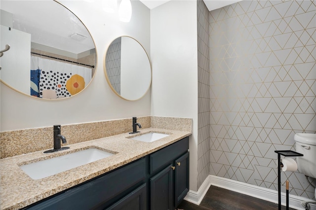 bathroom featuring toilet, vanity with extensive cabinet space, dual sinks, and hardwood / wood-style flooring