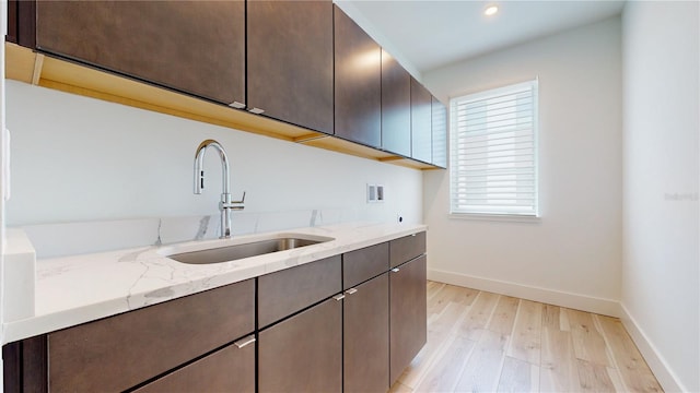 kitchen featuring dark brown cabinetry, light hardwood / wood-style floors, sink, and light stone counters