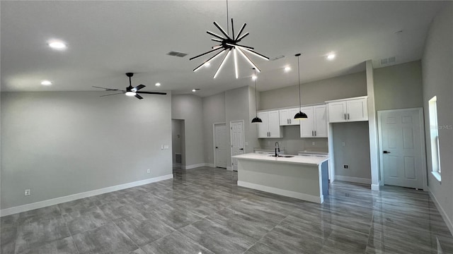 kitchen with pendant lighting, a kitchen island with sink, white cabinets, sink, and a towering ceiling