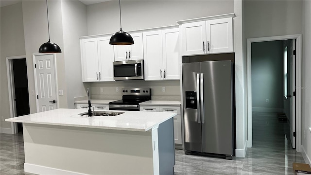 kitchen featuring a center island with sink, white cabinets, stainless steel appliances, and decorative light fixtures