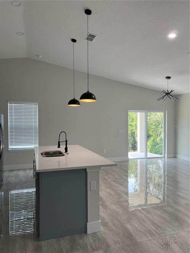 kitchen featuring sink, light stone counters, lofted ceiling, decorative light fixtures, and a kitchen island with sink