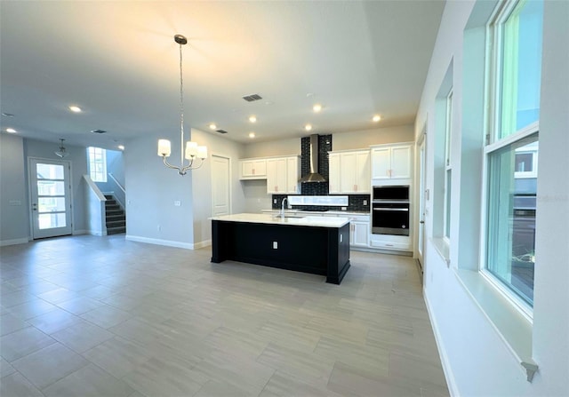 kitchen featuring white cabinetry, pendant lighting, a kitchen island with sink, and wall chimney range hood