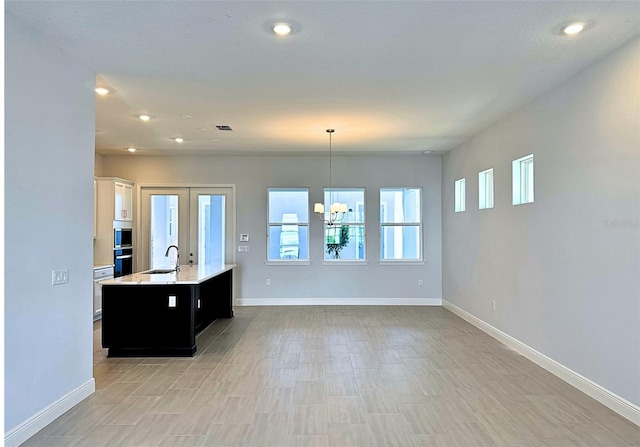 kitchen featuring pendant lighting, white cabinetry, a notable chandelier, a center island with sink, and french doors