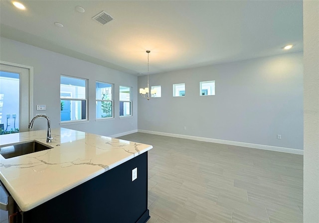 kitchen featuring pendant lighting, sink, an inviting chandelier, light stone counters, and an island with sink