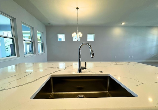 kitchen featuring hanging light fixtures, light stone countertops, sink, and a notable chandelier