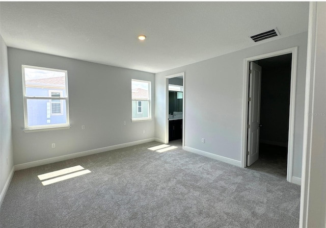 unfurnished bedroom with multiple windows, light colored carpet, and ensuite bathroom