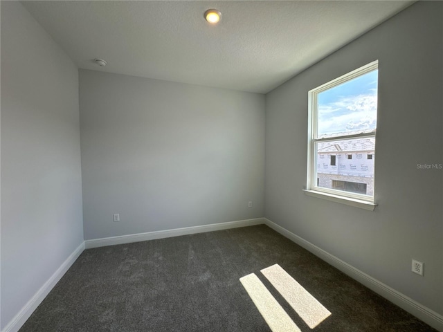 unfurnished room featuring a textured ceiling and dark colored carpet