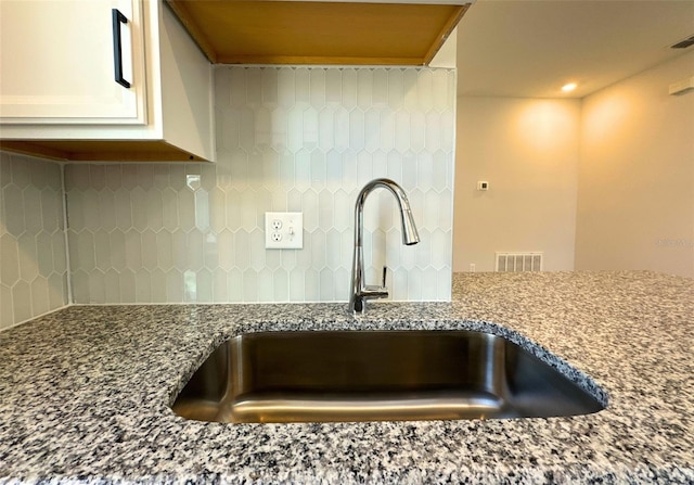 details with white cabinetry, sink, backsplash, and stone countertops