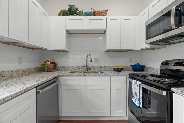 kitchen with light stone counters, stainless steel appliances, a sink, white cabinetry, and backsplash