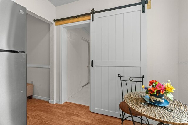 hallway featuring a barn door, light wood-type flooring, and baseboards