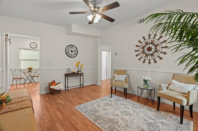 living area with a ceiling fan, visible vents, baseboards, and wood finished floors