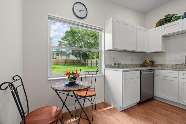 kitchen featuring white cabinets, stainless steel dishwasher, light wood-type flooring, light stone countertops, and tasteful backsplash