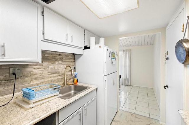 kitchen with white refrigerator, light tile flooring, backsplash, white cabinetry, and sink