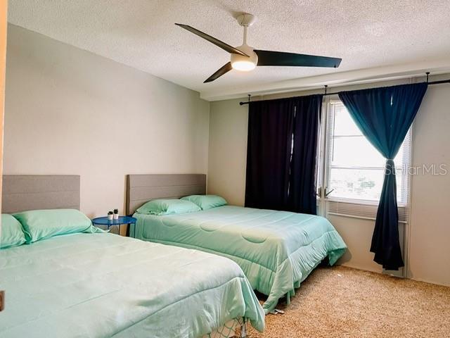 carpeted bedroom with ceiling fan and a textured ceiling