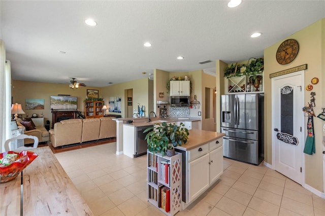 kitchen with light tile patterned floors, white cabinets, stainless steel fridge, and a kitchen island