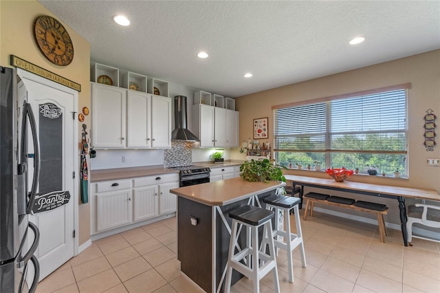 kitchen with wall chimney range hood, a kitchen island, decorative backsplash, electric range, and white cabinetry