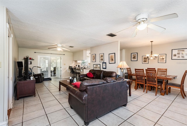 living room with ceiling fan with notable chandelier, light tile patterned flooring, and a textured ceiling