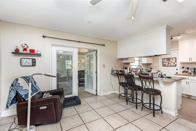 kitchen with decorative backsplash, kitchen peninsula, light stone countertops, white cabinets, and a breakfast bar area